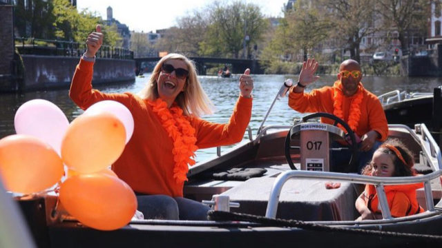 Mokumboot tugboat full of partygoers on the Amstel in Amsterdam during King&rsquo;s Day, decorated with orange, looking towards the Magere Brug.