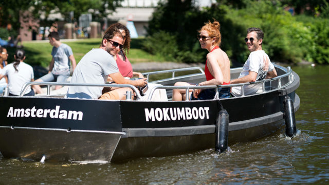 Two men and two women sailing on a sloop through the Amsterdam canals on a sunny day.