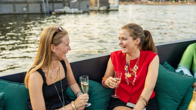 Gezelschap ontspant op een Mokumboot sloep aan de Amstel met uitzicht op Amsterdamse grachtenpanden