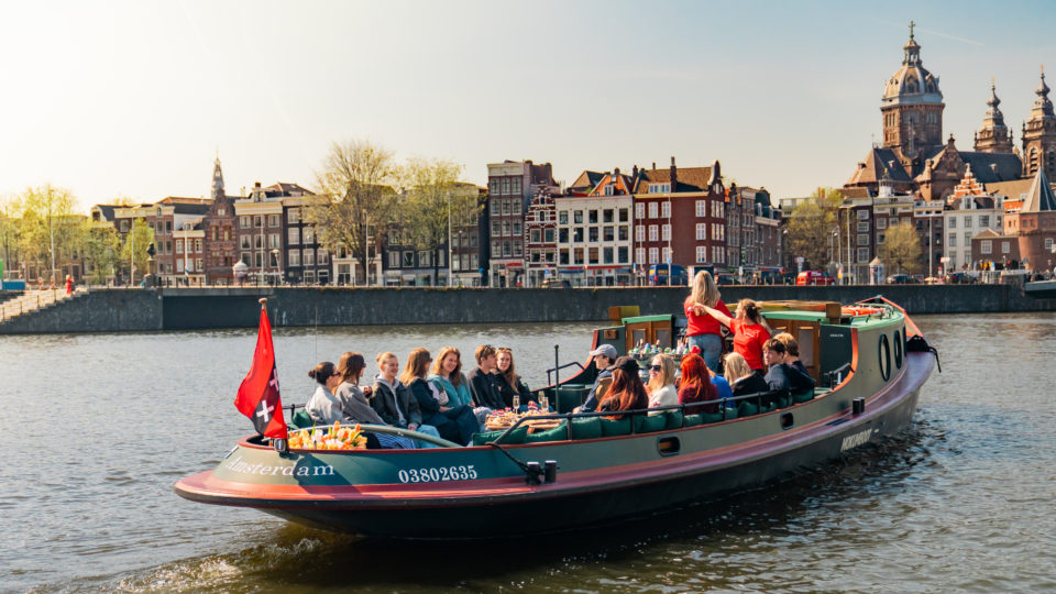Open boot met een groep mensen die genieten van de skyline van Amsterdam vanaf de grachten.