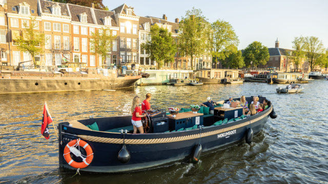 Mokumboot sloop on the water near the Magere Brug in Amsterdam, with a relaxed group enjoying the cruise.