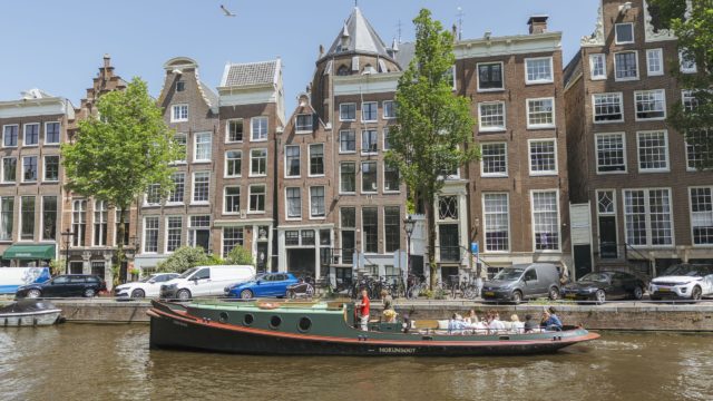 Mokumboot sleepboot met passagiers op de Amstel, langs de iconische Magere Brug in Amsterdam.